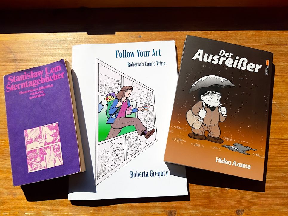 Drei Bücher auf einem Tisch. »Sterntagebücher« von Stanislaw Lem, »Follow your Art« von Roberta Gregory und »Der Ausreißer« von Hideo Azuma.
