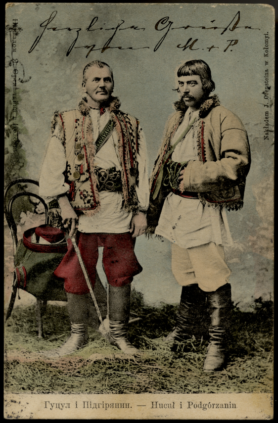 Auf der Postkarte sind zwei Männer in Stiefeln und traditionellem Gewand abgebildet. Einer von ihnen hält einen Degen in der Hand. Die Karte ist auf der Bildseite mit einem handschriftlichen Gruß versehen.