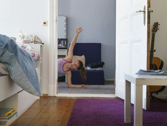Ein Mädchen macht Gymnastik, sie ist halb durch eine Tür zu sehen.