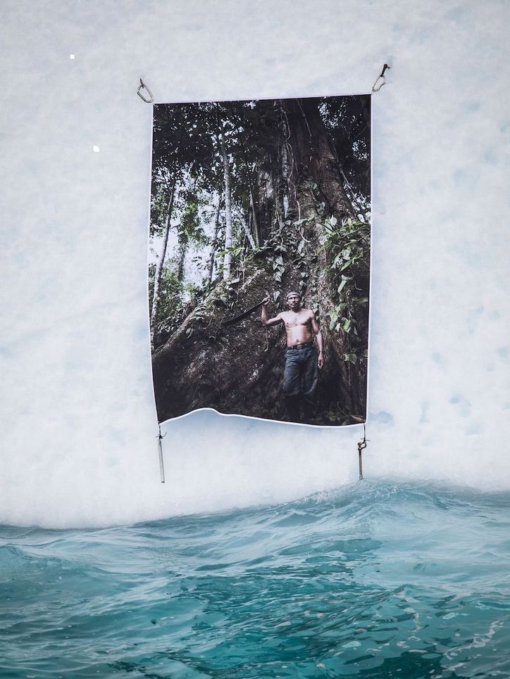 Foto eines jungen Mannes mit freiem Oberkörper im Wald. Das Foto ist an einer Schneewand über dem Wasser angebracht.