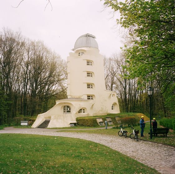 Ein heller Turm mit Treppeneingang, vielen Fenstern und einer Kuppel in einem Park.