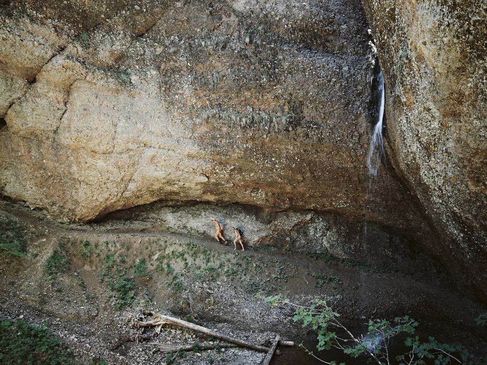 Zwei unbekleidete Wanderer auf einem Pfad unter einem riesigen Felsvorsprung.