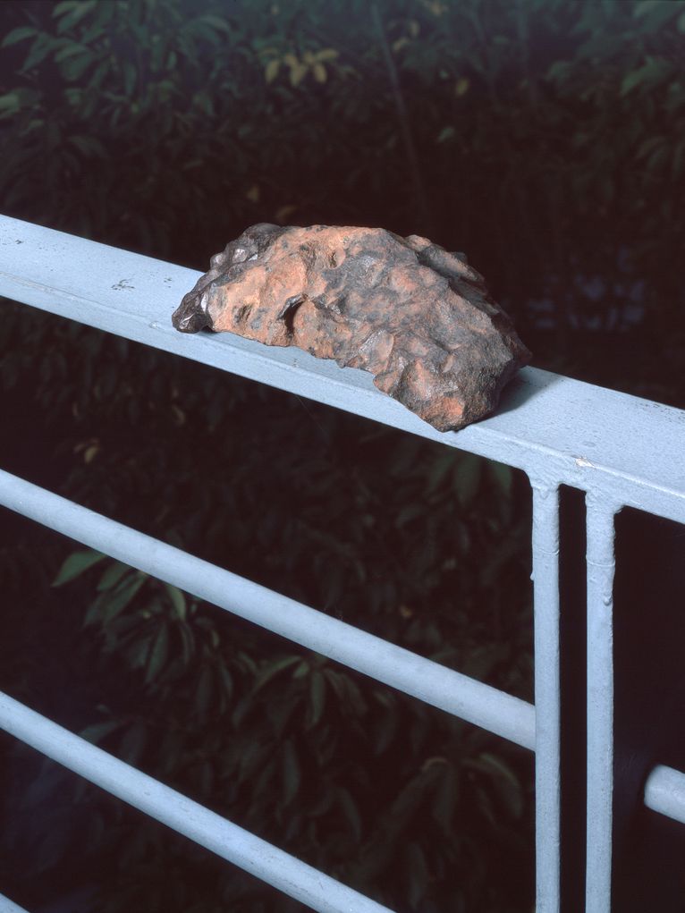 Rötlich-anthrazitfarbener Meteorit auf einem Metallgeländer.