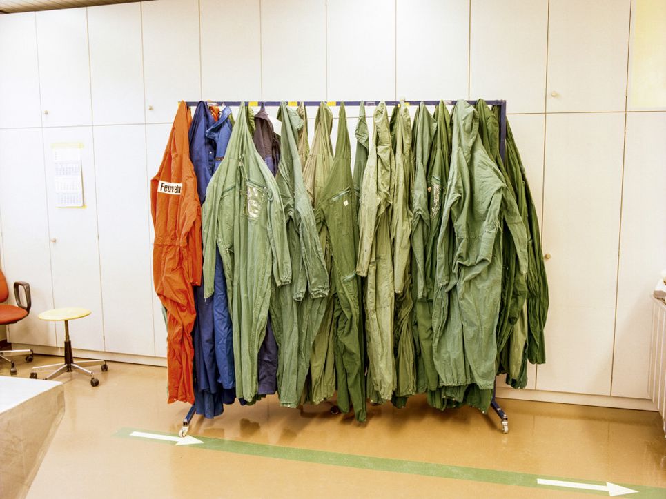 Kleiderständer mit grünen, orangenen und blauen Schutzanzügen.