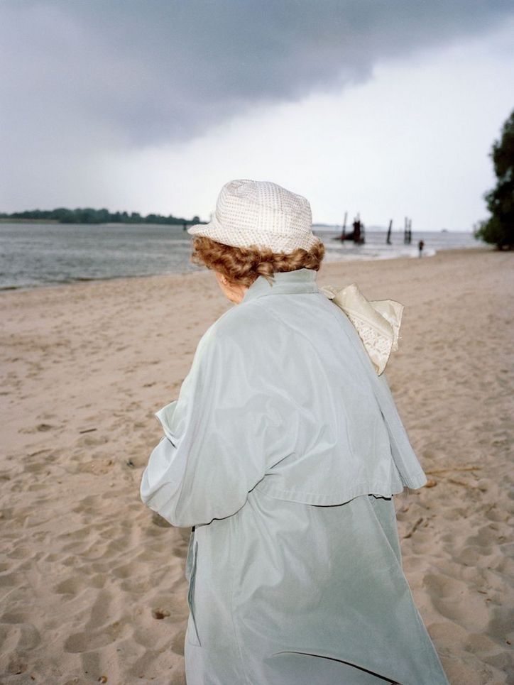 Eine alte Frau mit Hut am Sandstrand eines Flusses.