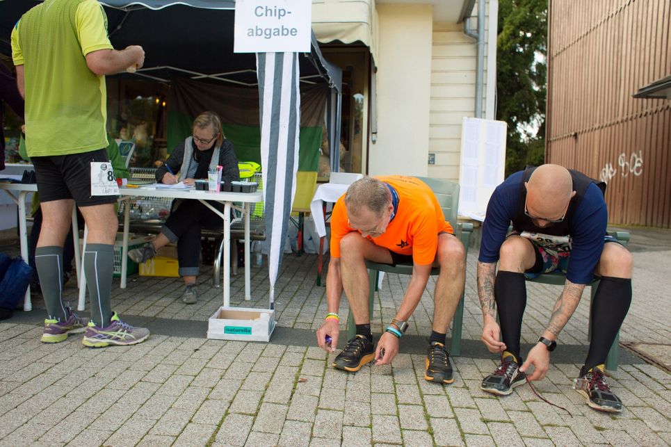 Hans G. Drexler sitzt vornübergebeugt mit einem weiteren Läufer neben einem Pavillon mit der Aufschrift: Chipabgabe.