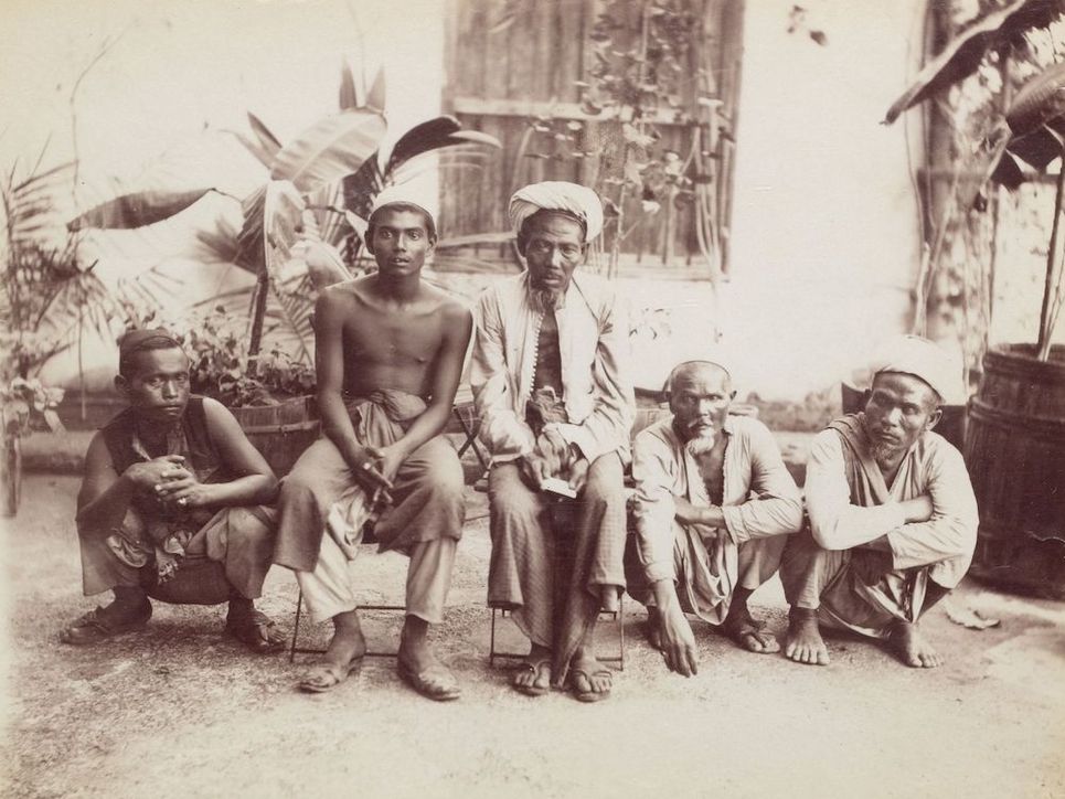 Historische Fotografie von zwei jüngeren und drei älteren Männern. Einige von ihnen sitzen in der Hocke.
