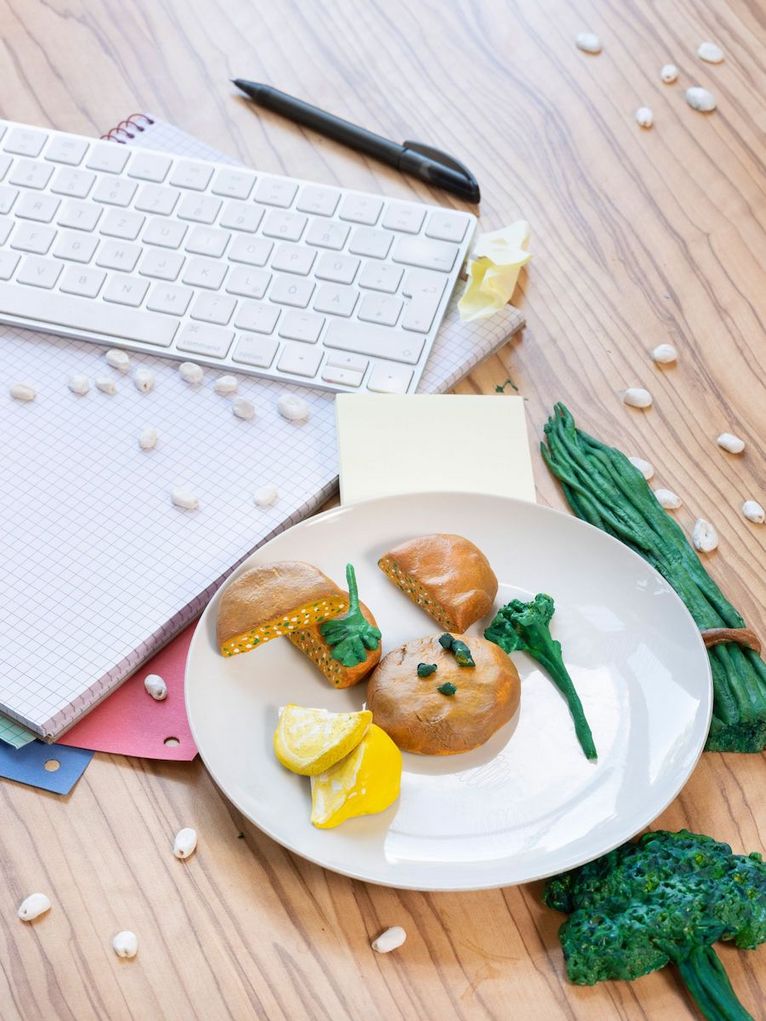 Lupinenbratlinge, grünes Gemüse und Zitronenscheiben aus Plastik auf einem Teller neben einer Tastatur und Papier.