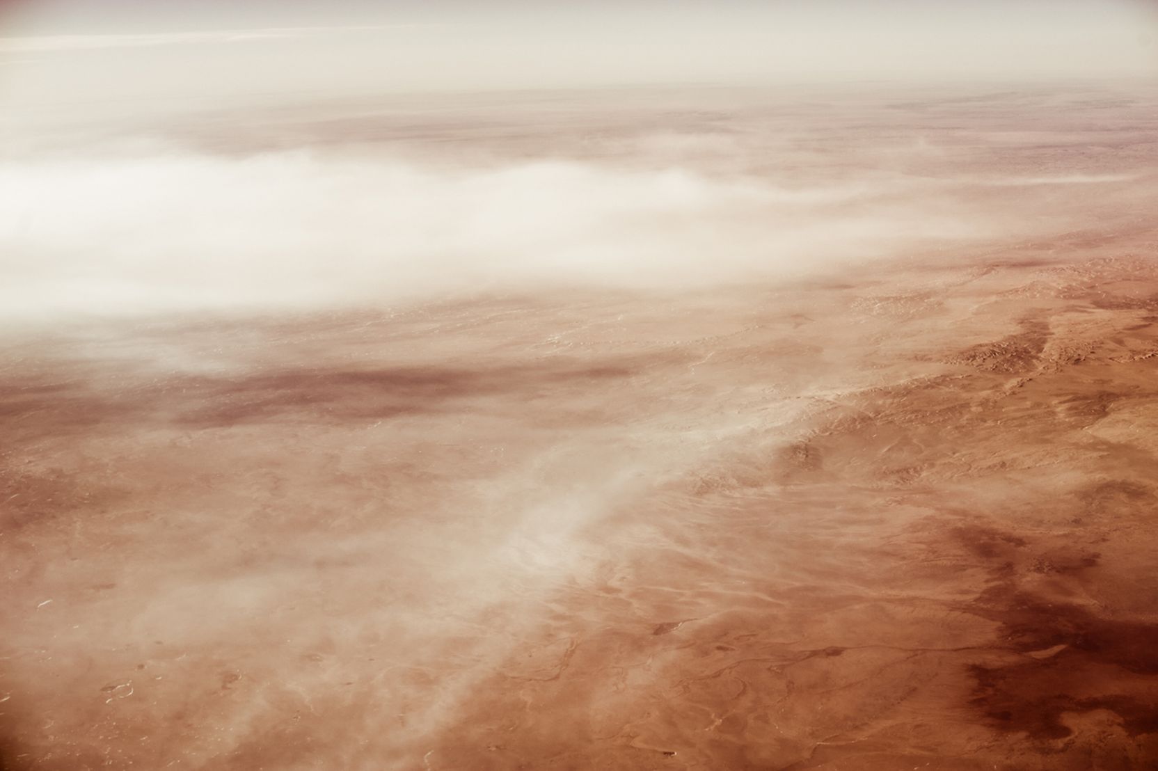 Luftbildaufnahme einer sandigen Hügellandschaft mit feinen Wolken