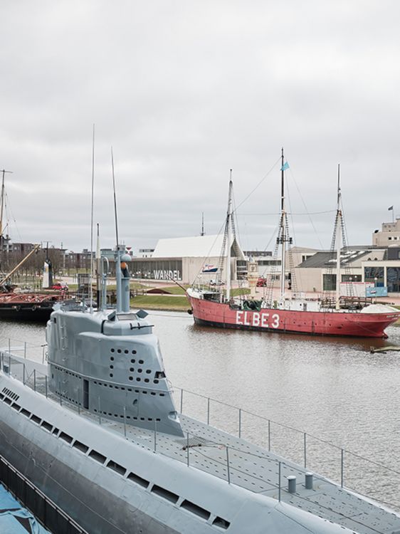 Ein graues Schiff liegt im Wasser, dahinter ein roter Dreimaster im Außenbereich des Deutschen Schifffahrtsmuseums