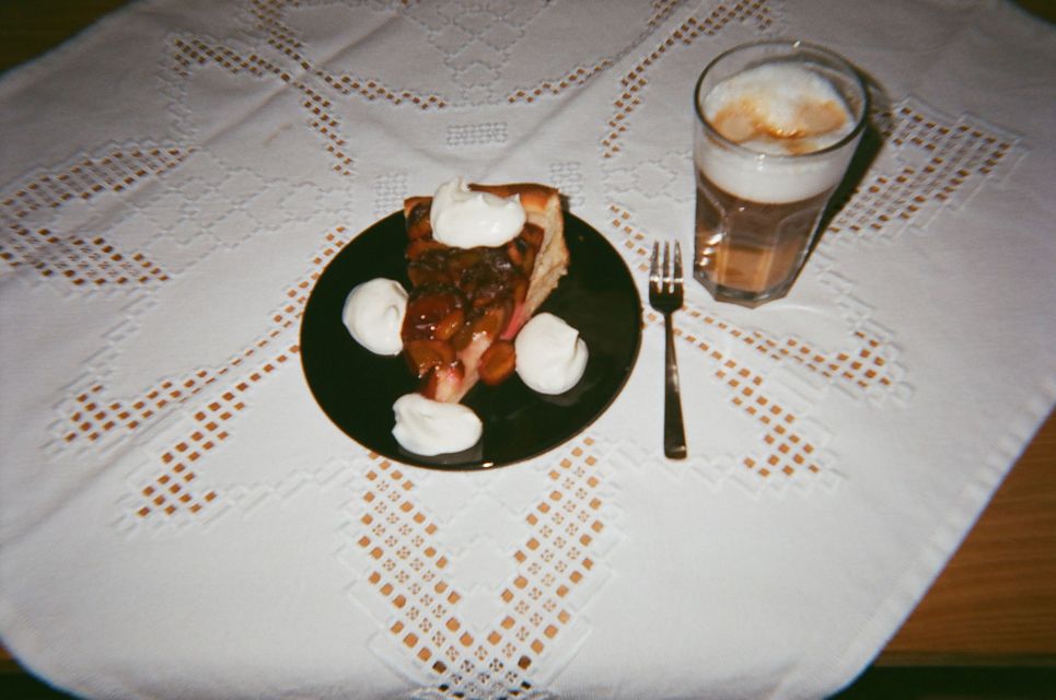 Zwetschenkuchen mit Sahne und Latte Macchiato im Glas auf einer feinen weißen Tischdecke.