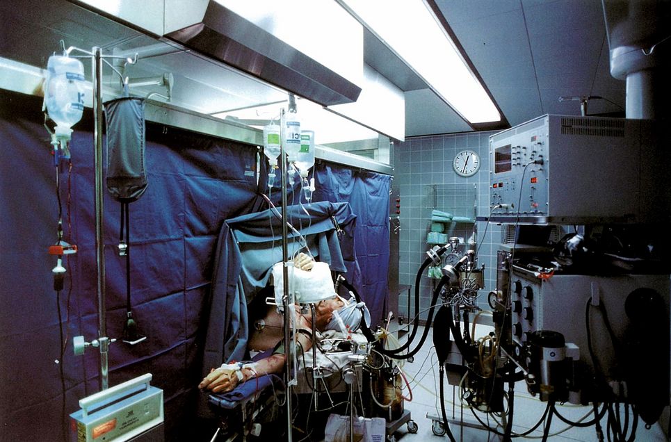 Verwundeter Patient auf einer Krankenhausliege, der von Geräten versorgt wird.