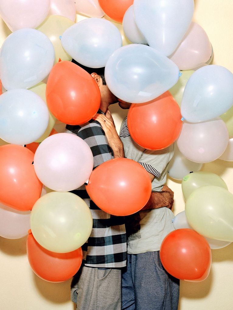 Zwei Männer, die sich halb verdeckt von bunten Luftballons küssen.