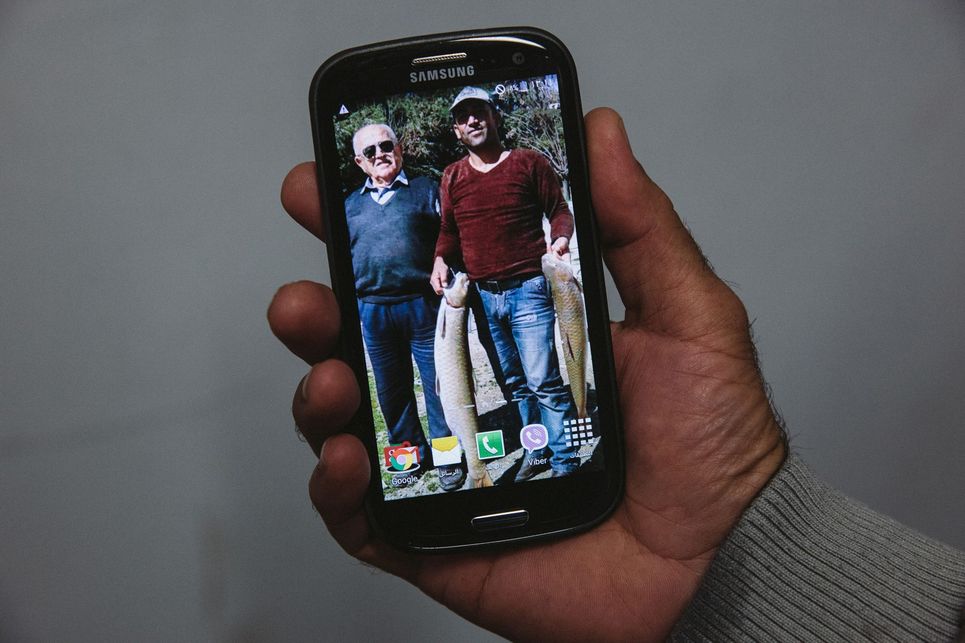 Ein älterer Mann und ein jüngerer mit zwei großen Fischen auf dem Display eines Handys.