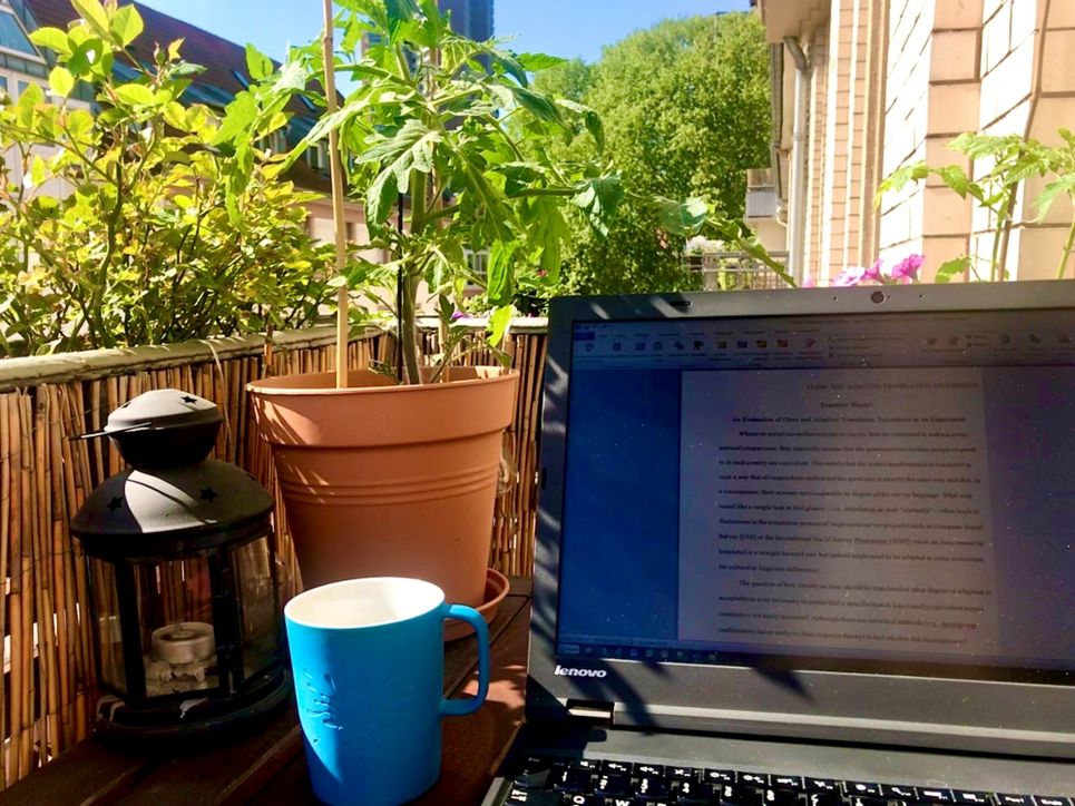 Laptop und Tasse auf einem sonnigen Balkon mit Pflanzen.
