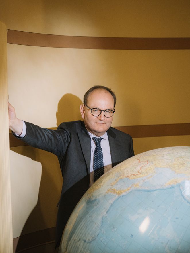 Ottmar Edenhofer vor einem großen Globus, eine Hand an einem Heizkörper.
