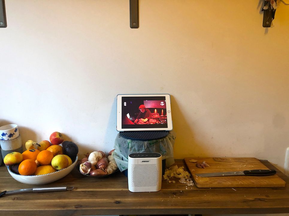 Arbeitsplatte mit Obst, Messer, Brett, Knoblauch, einer Box und einem DJ, der auf einem iPad zu sehen ist.