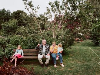 Eine ältere Frau und ein älterer Mann auf einer Bank in einem Garten mit zwei kleinen Mädchen.