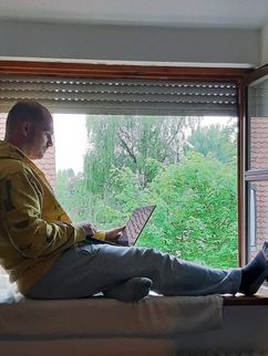 Patrick Marcineck sitzt im Fensterrahmen mit Laptop auf dem Schoß.
