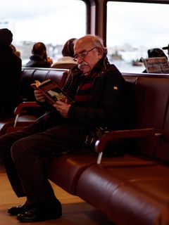Ein älterer Herr sitzt mit einem Buch in der Hand in einem Schiff unter Deck.