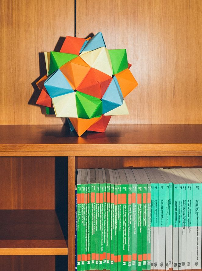 Geometrische Papierfigur auf einem kleinen Bücherregal.