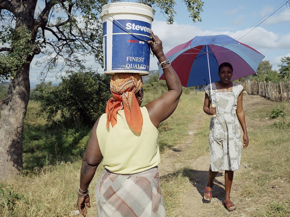 Eine Frau trägt einen Eimer mit Wasser auf dem Kopf