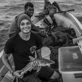 Der Fotograf Tom Vierus auf einem Boot mit zwei weiteren Männern und einem kleinen Fisch in den Händen. 