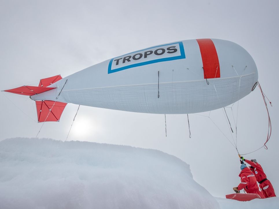 Der Fesselballon mit der Aufschrift »Tropos« steigt in die Höhe, zwei Personen halten eine Schnur.