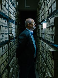 Michael Farrenkopf, der stellvertretende Direktor des Deutschen Bergbau-Museums Bochum, steht in einem schwach erleuchteten Raum zwischen zwei hohen Regalen, in denen sich mit Nummern beschriftete Kästen befinden. Er blickt durch eine Lücke im Regal, durch die Licht eindringt.