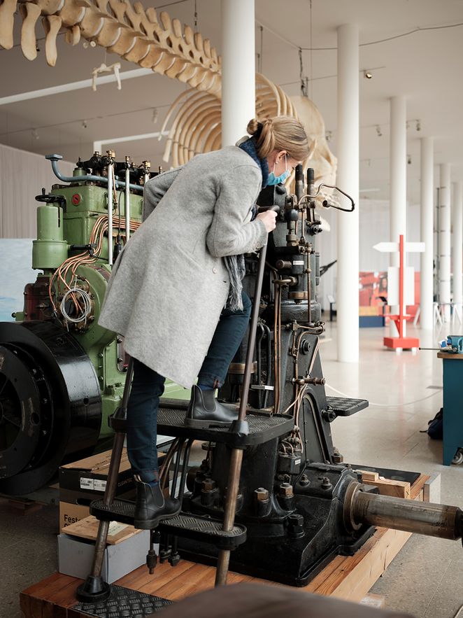 Im Deutschen Schifffahrtsmuseum steht Kathrin Kleibl auf einer Leiter und untersucht den Viertaktmotor.