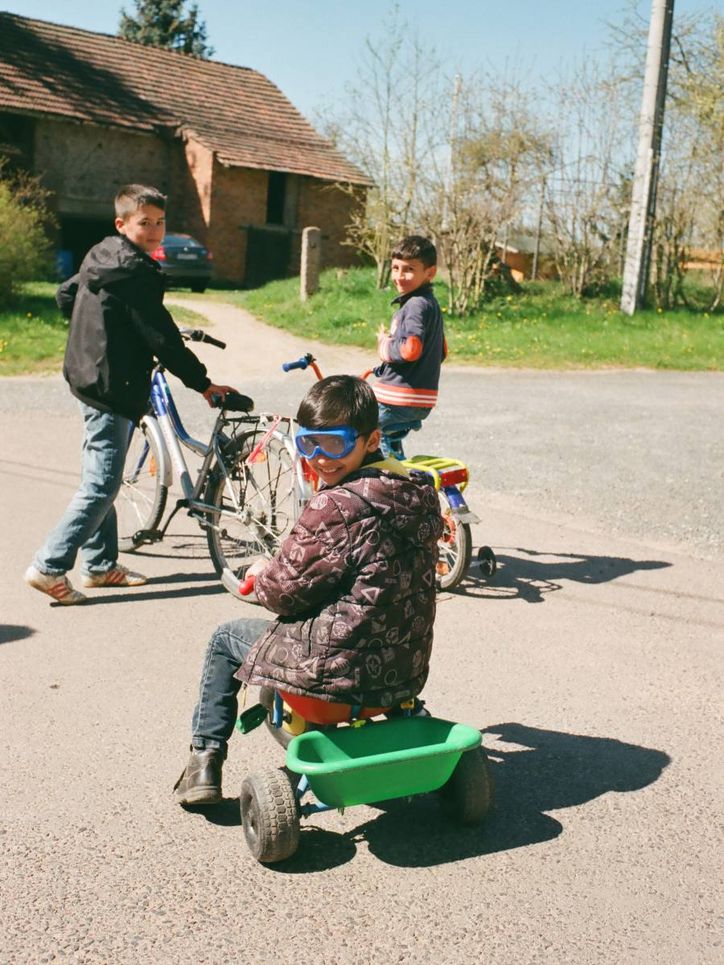 Drei Kinder mit zwei Fahrrädern und einem Bobbycar.