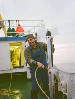 Alexander Bartholomä mit Wasserschlauch an Deck eines Schiffes.