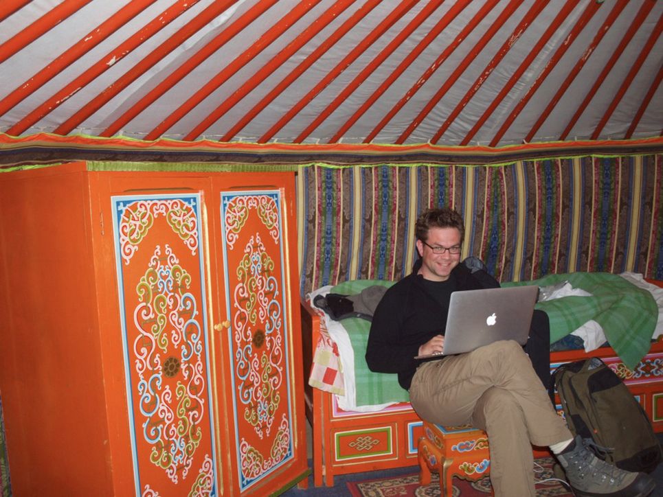 Thomas Müller sitzt mit Laptop in einer von bunten Stoffen ausgekleideten Jurte.
