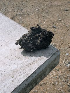 Anthrazitfarbener Meteorit am Rand einer Betonplatte.