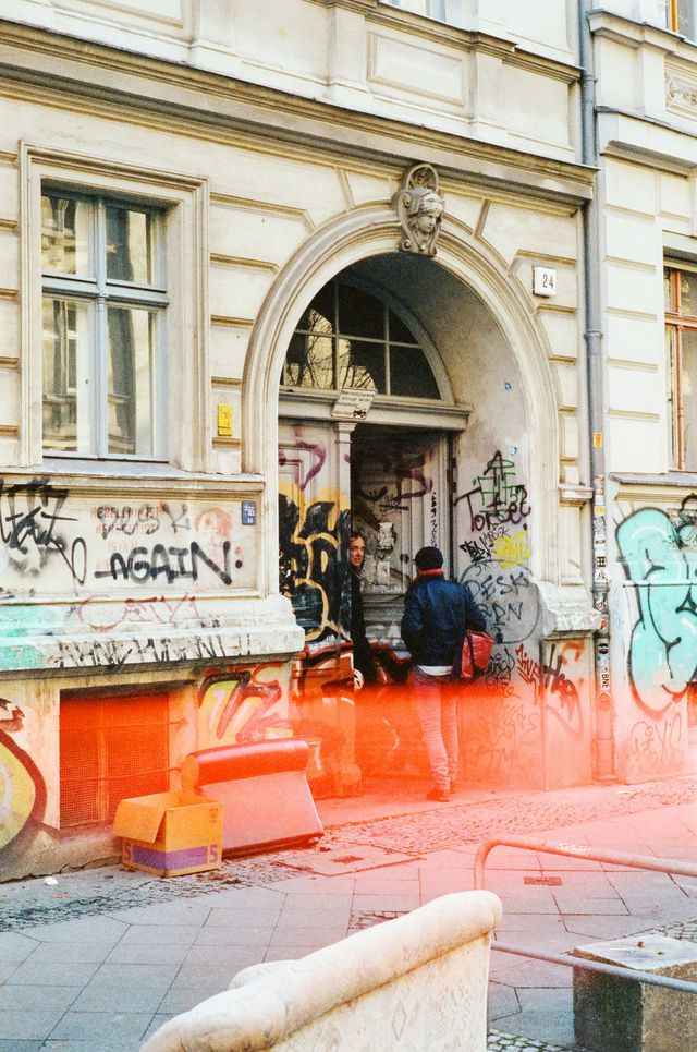 Zwei Personen in der Tür eines Altbaus, der mit Graffiti besprüht ist.