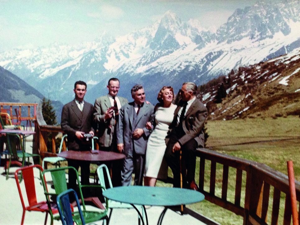 Vier Männer und eine Frau auf einer Terrasse, Bergpanorama im Hintergrund.