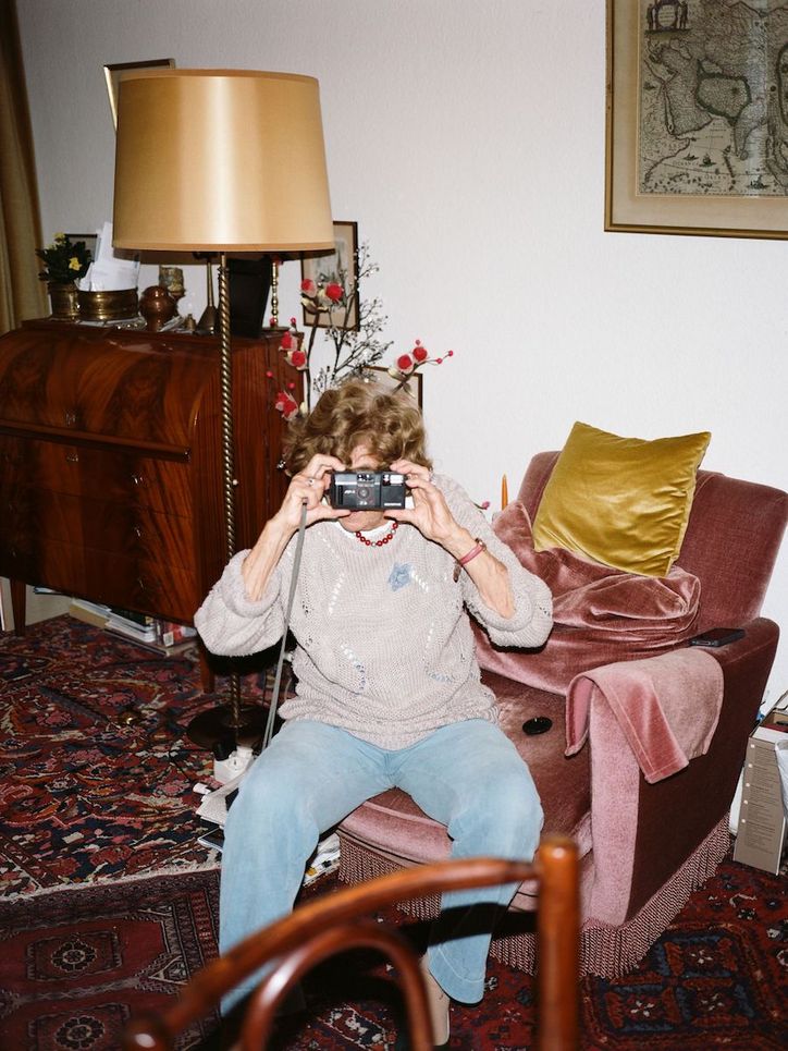 Eine alte Frau sitzt auf einem Sessel im Wohnzimmer und fotografiert mit einer Kamera mit Sucher.