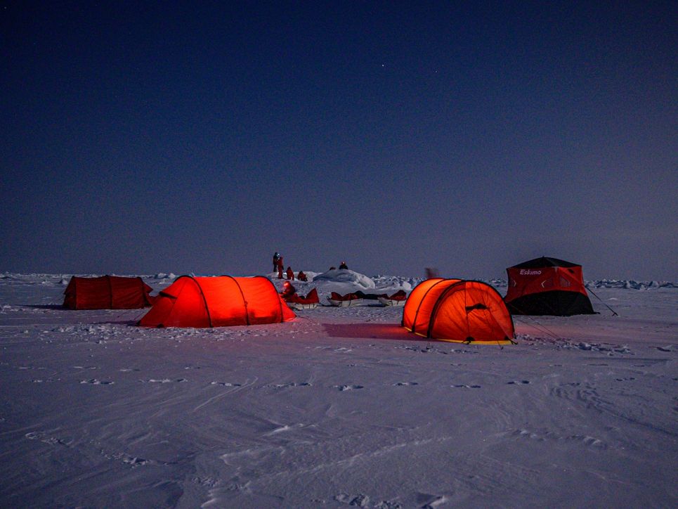 Orangene, von innen erleuchtete Zelte, Personen auf der Eisfläche.