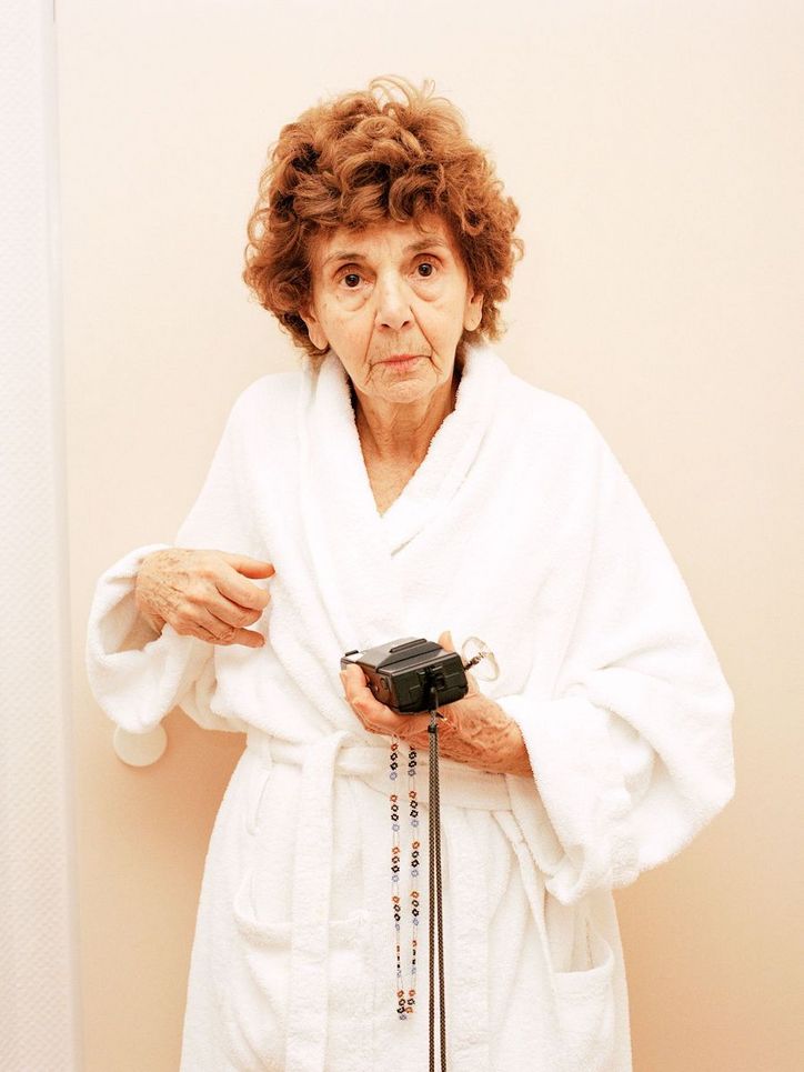 Eine alte Frau im weißen Bademantel mit einer Kamera in der Hand.