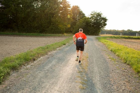 Der Marathonforscher läuft einen Feldweg entlang, er ist von hinten zu sehen.
