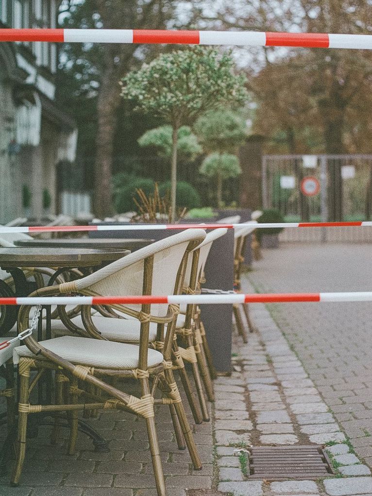 Stühle und Tische eines Cafés im Freien, im Vordergrund rot-weißer Absperrband 