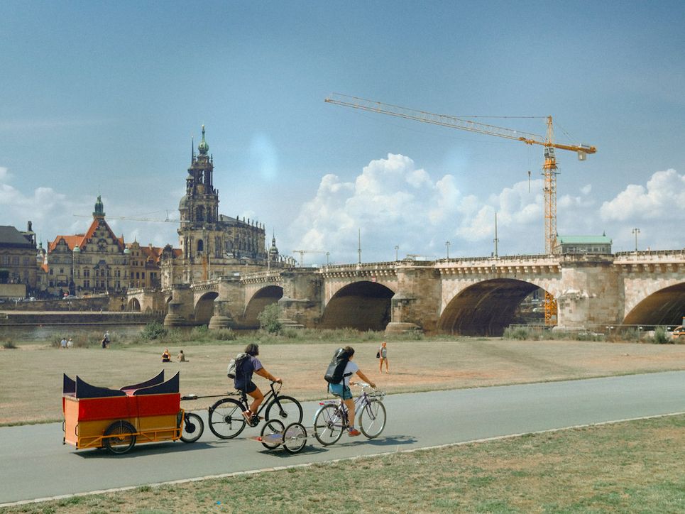 Zwei Radfahrende mit Anhängern, vor der Dresdener Altstadtkulisse.