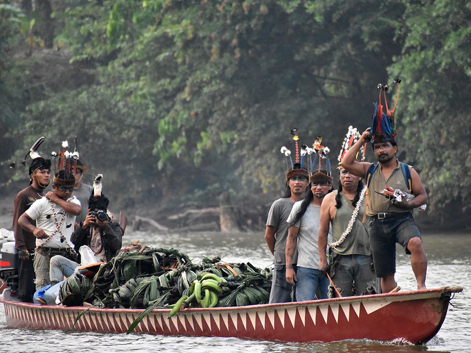 die Jäger der Kichwa kommen mit einem Boot voller Beute zurück. Sie stehen auf diesen und tragen besonderen Kopfschmuck. Leibniz Magazin. 