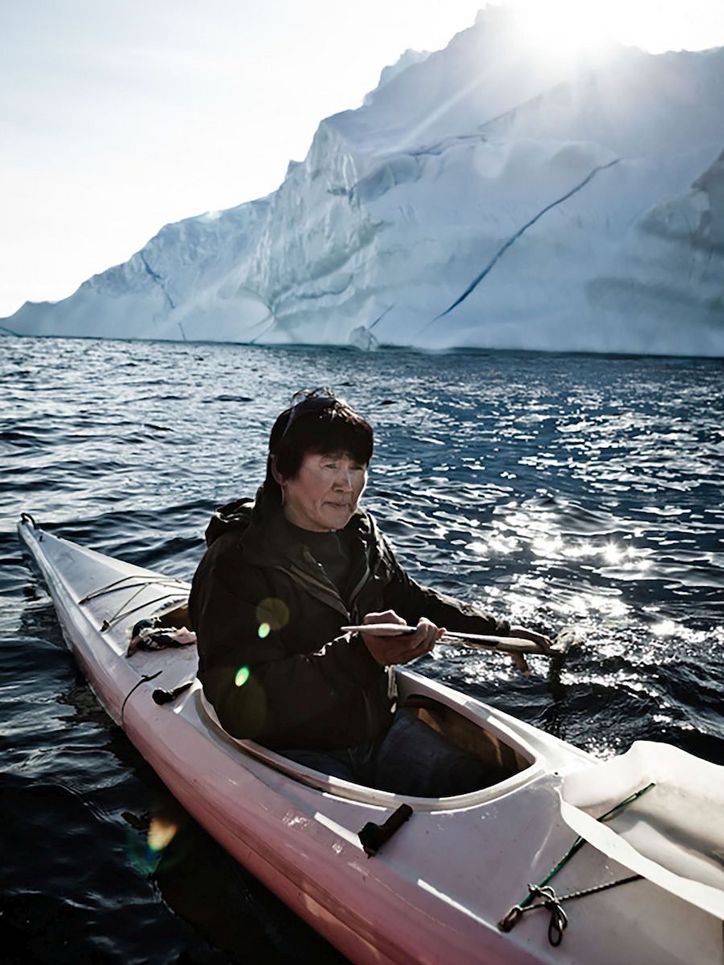 Frau in einem Kajak vor einem Eisberg.