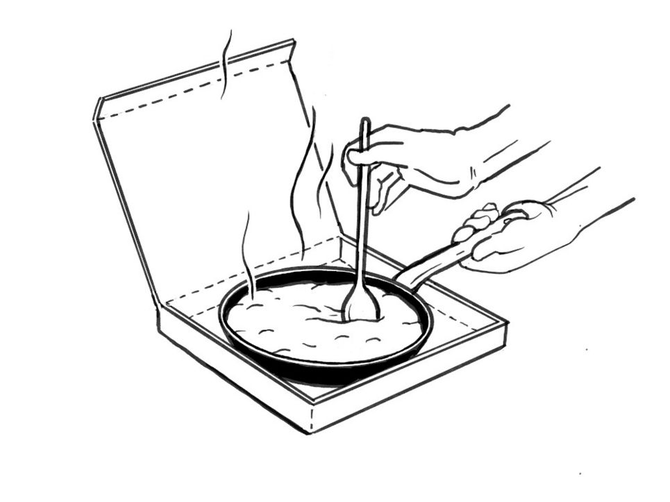 Eine Pfanne steht in einem Pizzakarton, das dampfende Essen wird mit einem Kochlöffel umgerührt.