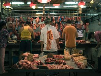 In einer Markthalle ist Fleisch aufgehängt und liegt auf Tischen, Menschen machen sich daran zu schaffen.