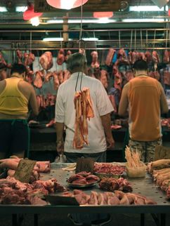 In einer Markthalle ist Fleisch aufgehängt und liegt auf Tischen, Menschen machen sich daran zu schaffen.