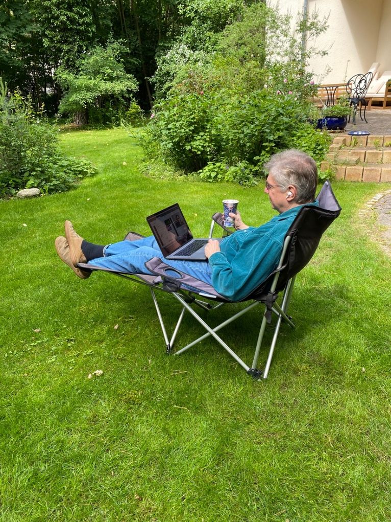 Matthias Steinmetz im Campingstuhl mit Laptop, Getränk und Headset im Garten.
