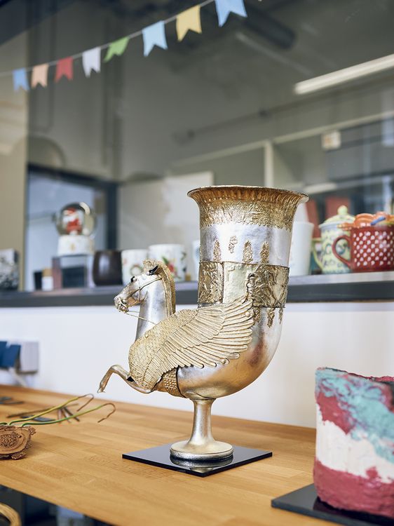 Eine gebogene Vase aus schimmerndem Metall mit Pferdekopf und Pferdebeinen.