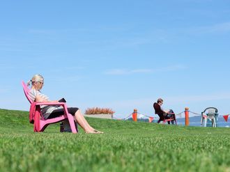 Lesende Personen auf Gartenstühlen auf einer grünen Wiese mit Ausblick.